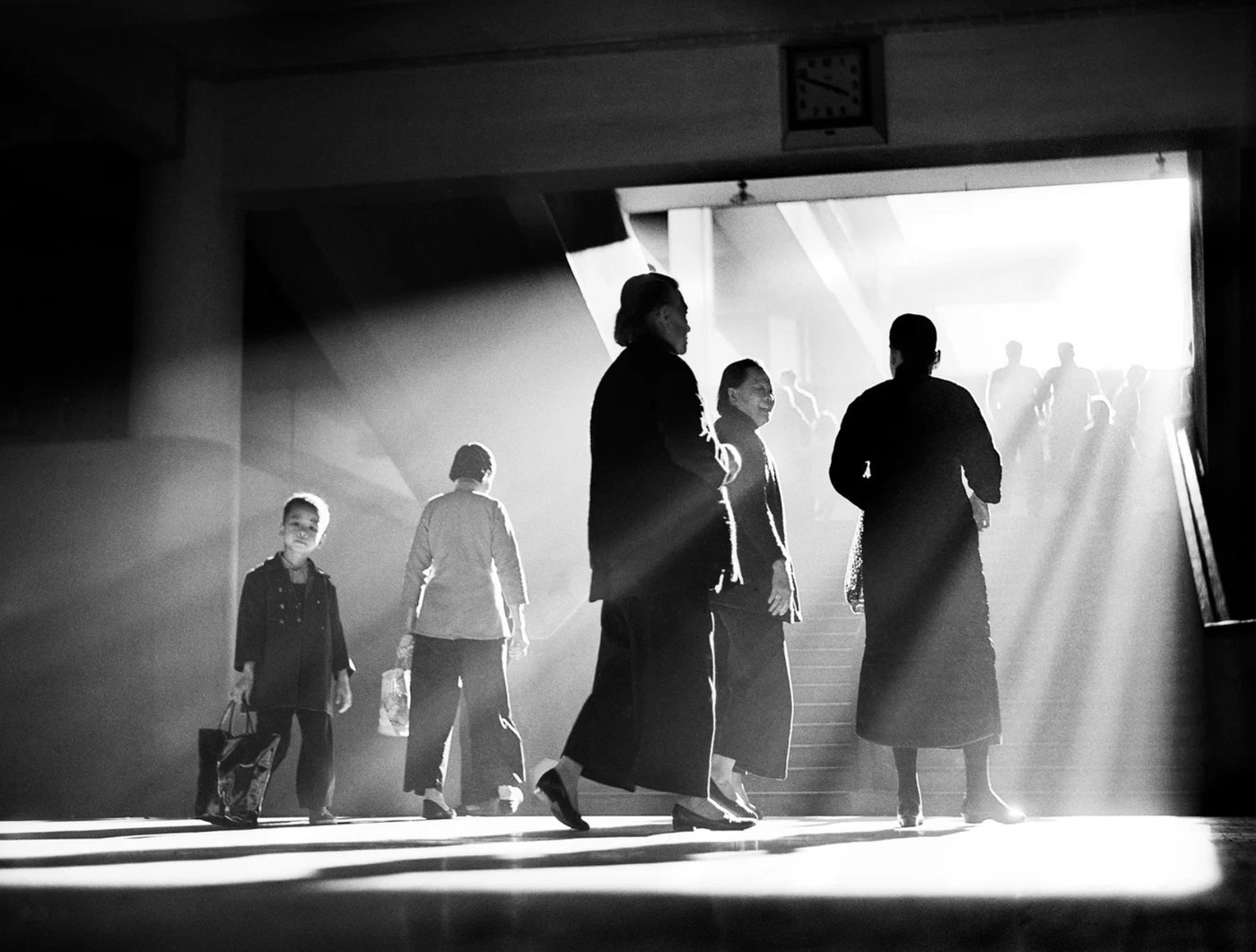 Afternoon Chat, de Fan Ho, 1959 — família em silhueta atravessando um saguão iluminado por trás, com um relógio na parede